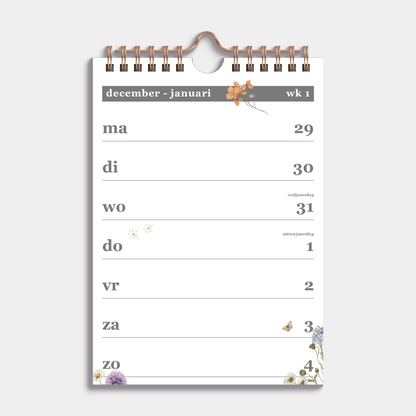 Weekkalender 2026 in A5 formaat met een subtiele print van weidebloemen, gebonden in een koperkleurige metalen spiraal en hanger – binnenwerk met weekoverzicht.